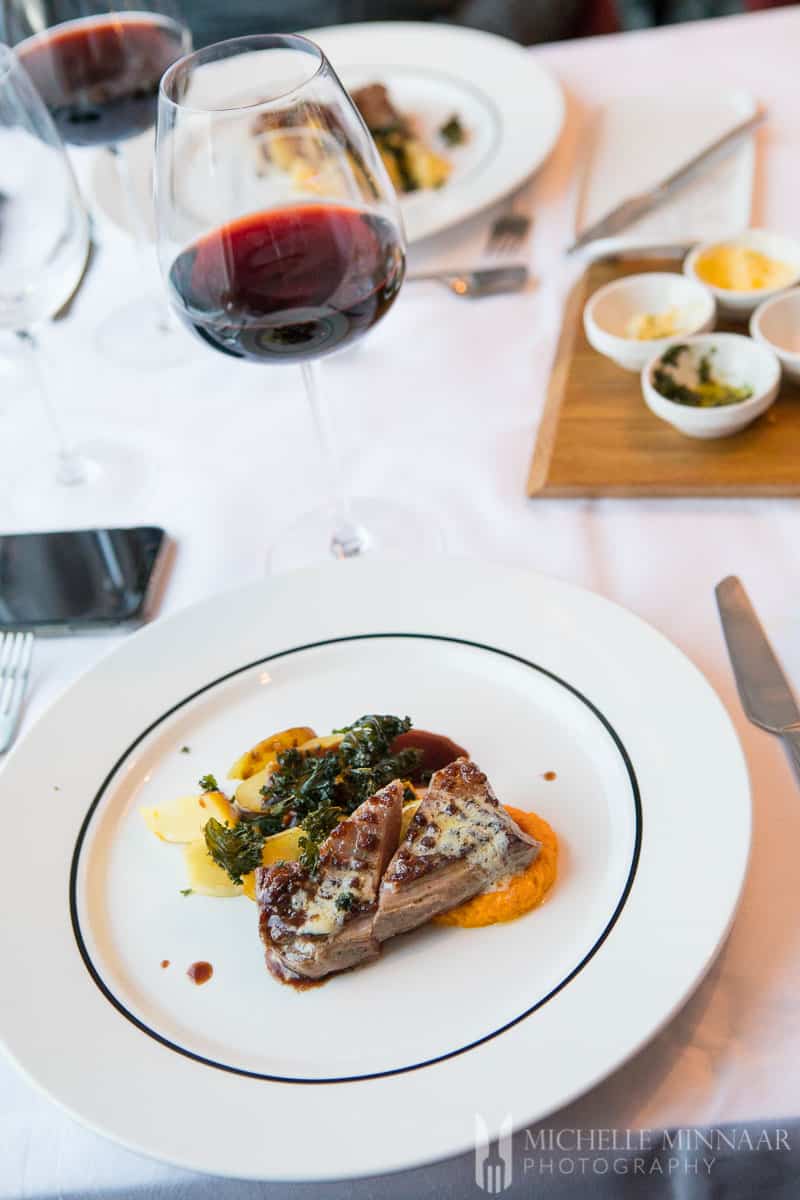 A lamb rump on a white plate with a glass of red wine 