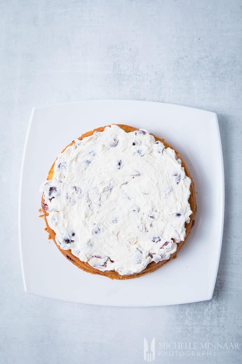 A layer of cake with frosting on top for a cherry bakewell cake