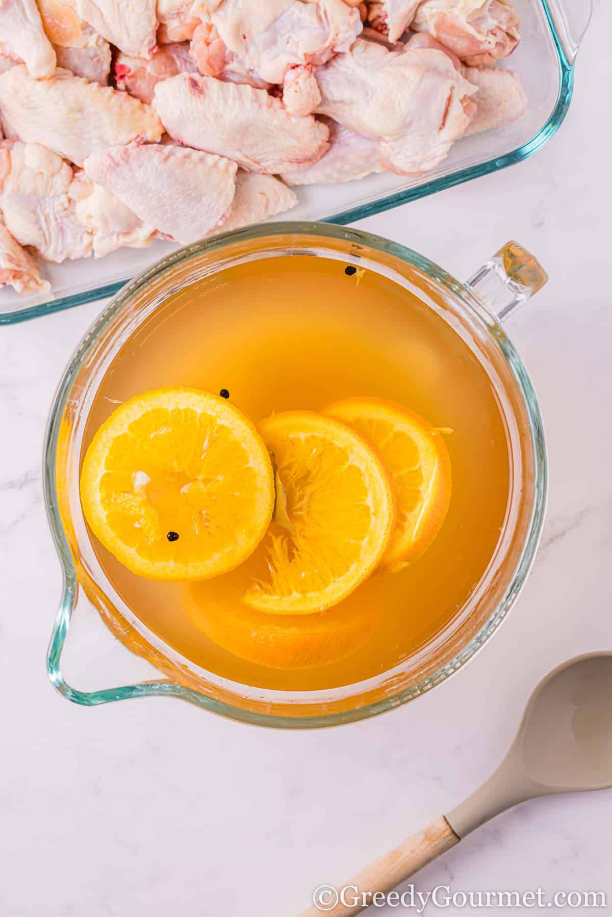 Brine in a glass jug next to a dish filled with raw chicken.