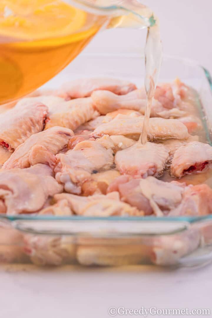 Pouring brine into a dish of raw chicken.