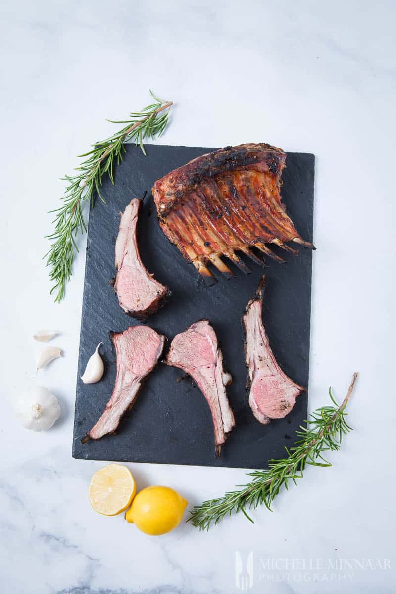 A rack of lamb and smaller pieces of bbq rack of lamb on a marble slab 