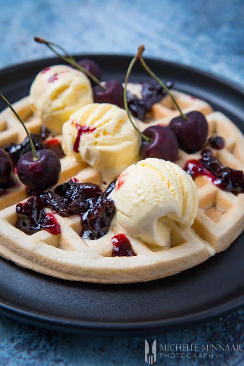 A close up of dairy free waffles with ice cream and cherries on top 