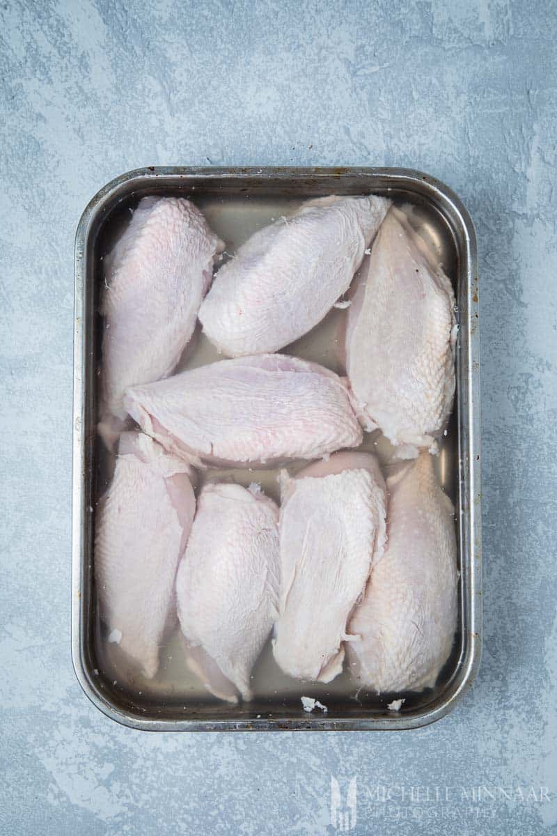 Raw chicken breasts in brining liquid in a pan