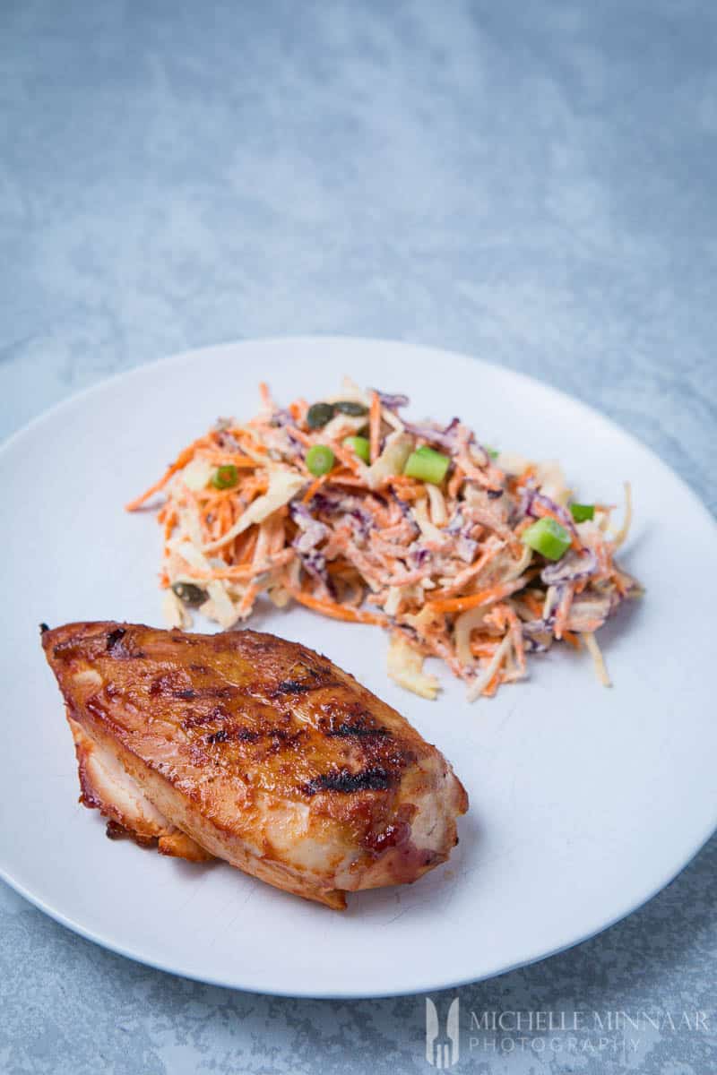 A brined chicken breast and vegan coleslaw on a white plate