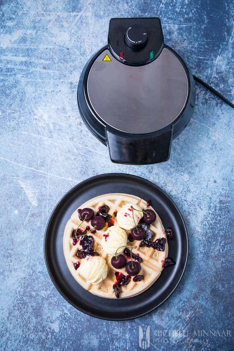 dairy free waffles on a plat with the waffle maker next to it 