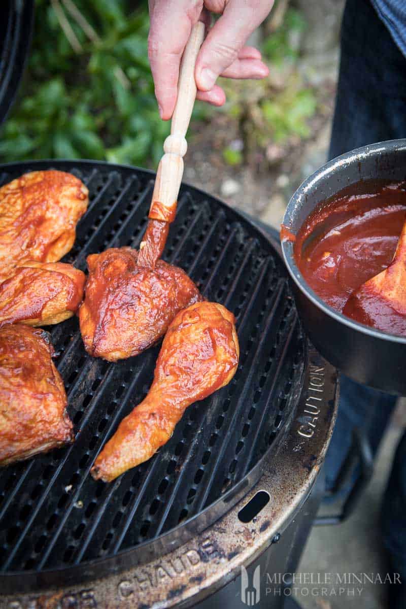 Chicken Drumsticks being sauced with bbq sauce on a grill 