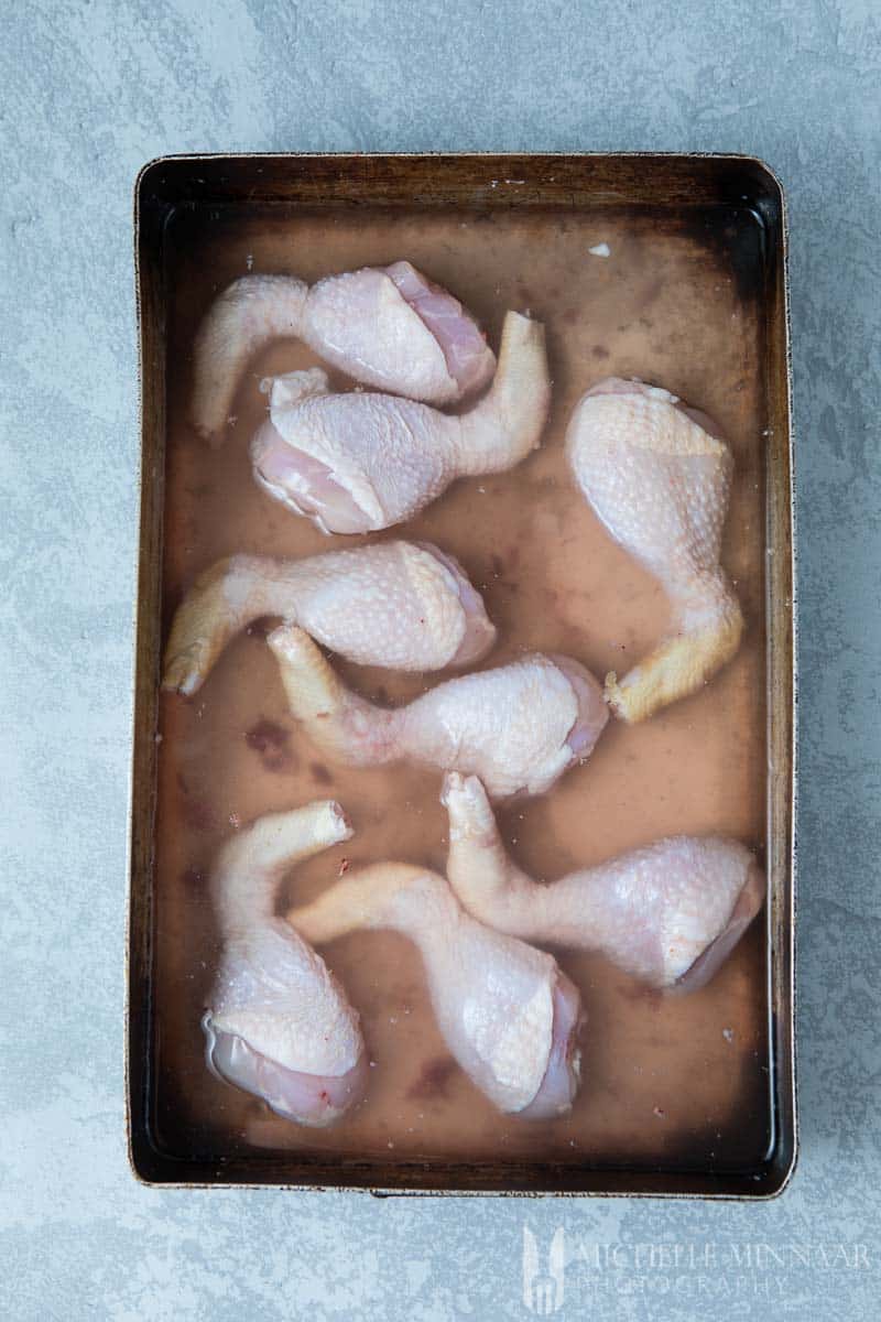 Raw Chicken Drumsticks in a pan full of liquid