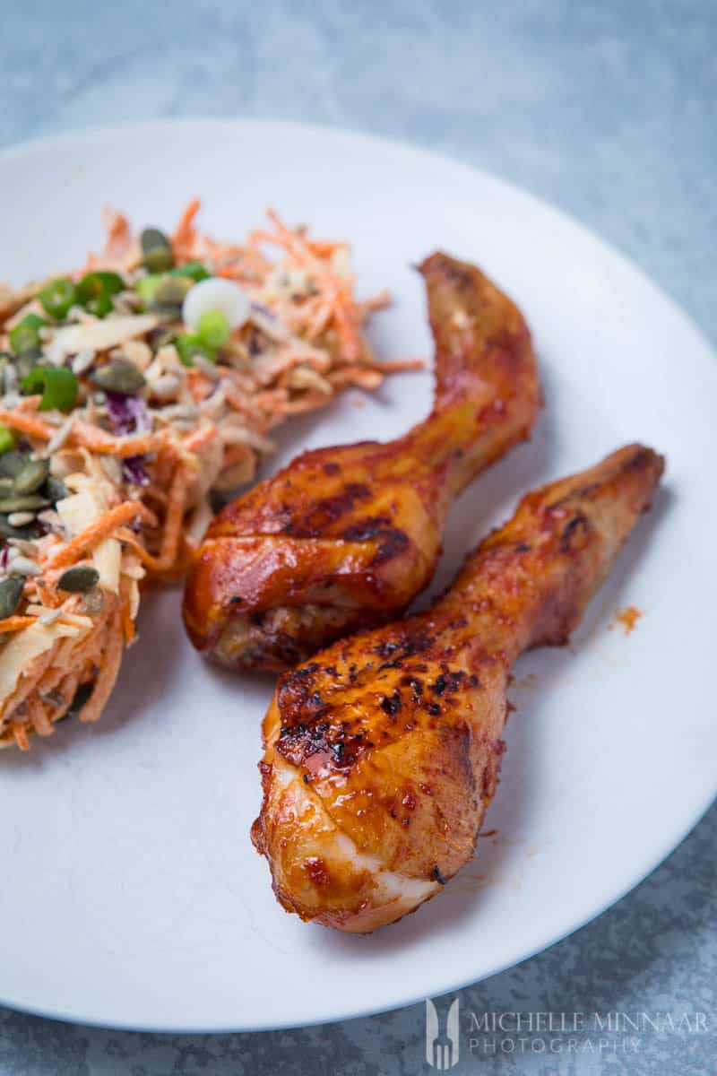 A close up of smoked chicken drumsticks on a plate with coleslaw