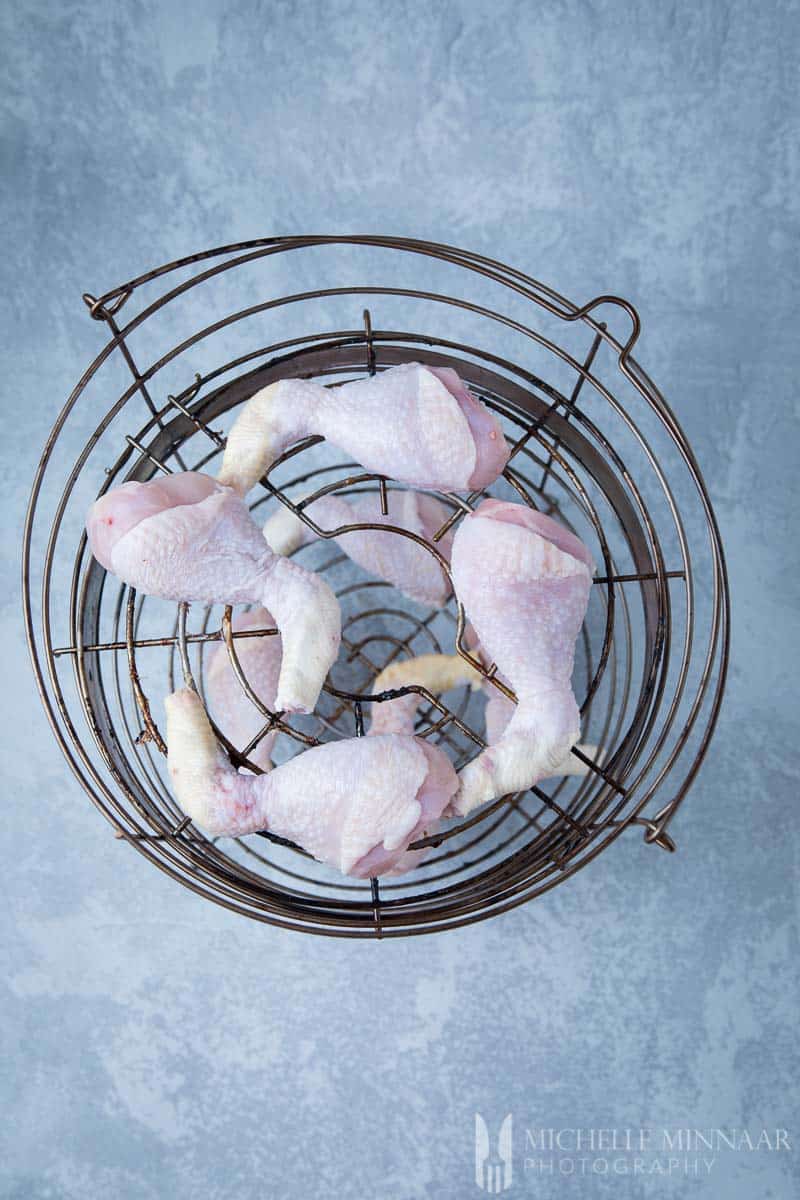 Raw chicken in a meta basket ready to make brined chicken drumsticks