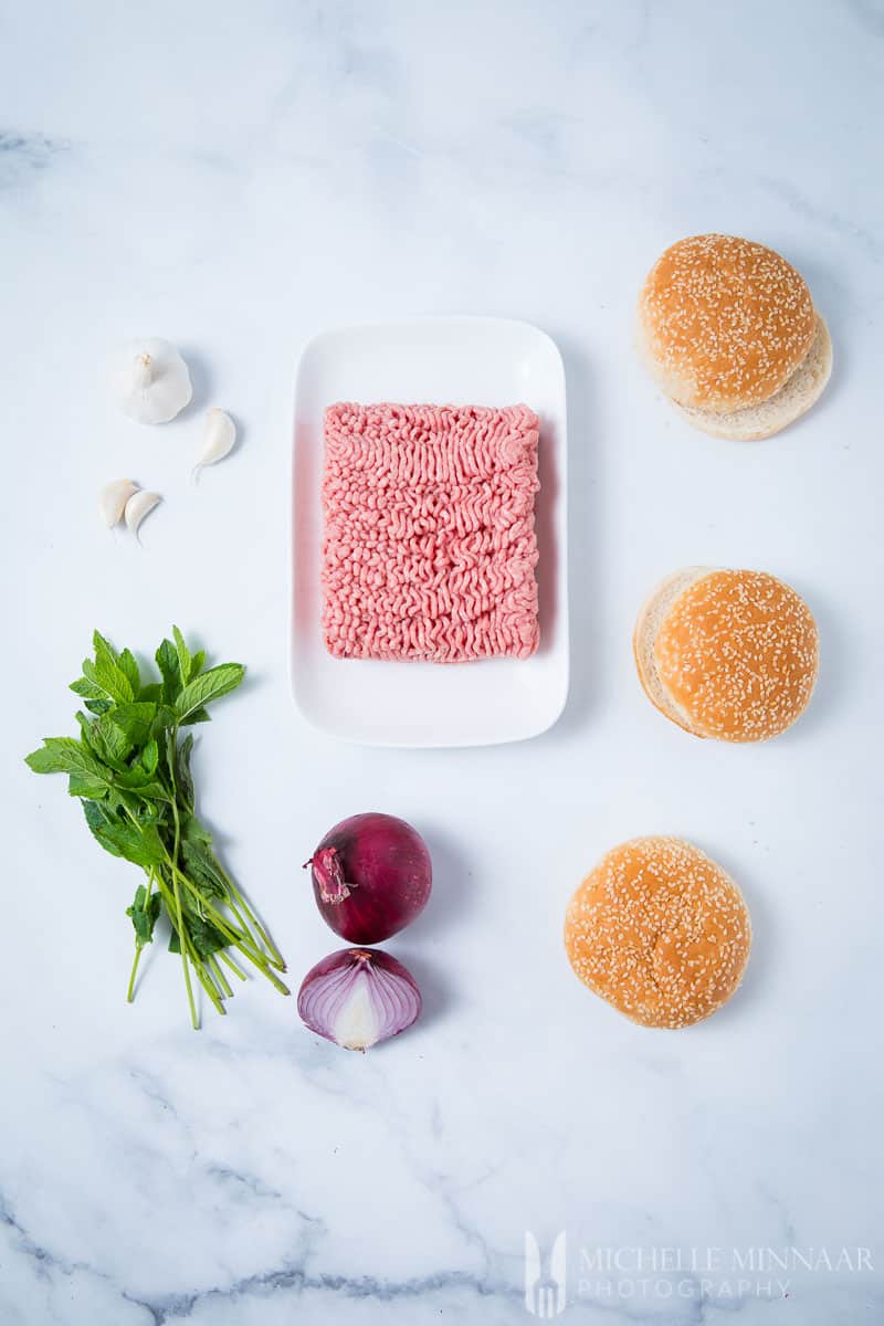 The ingredients for minted lamb burgers : raw ground lamb, onions, buns, mint sprigs, garlic