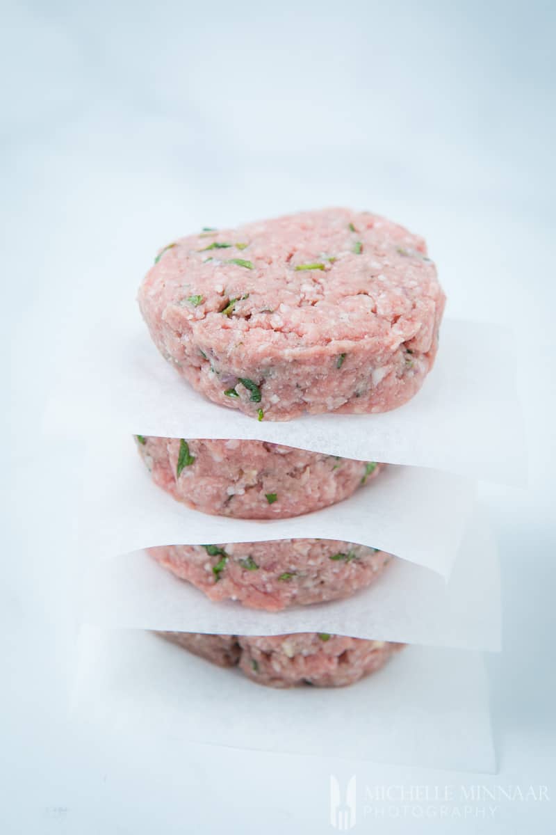 A close up of raw minted lamb burgers with paper in between each burger