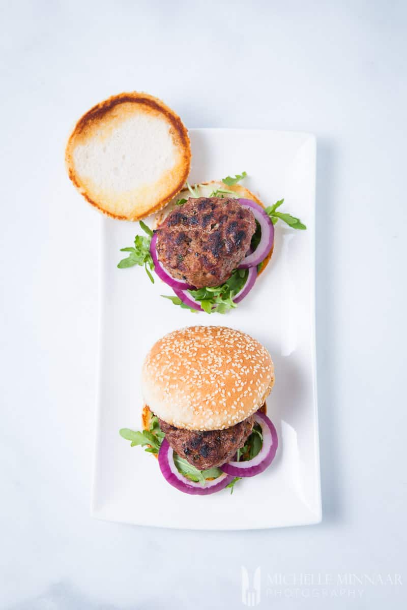 Two minted lamb burgers on a plate, one with the bun off 