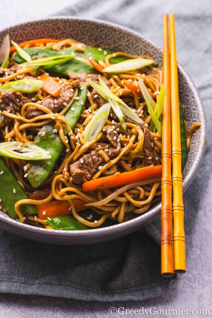 Beef chow mein in a bowl with chopsticks.