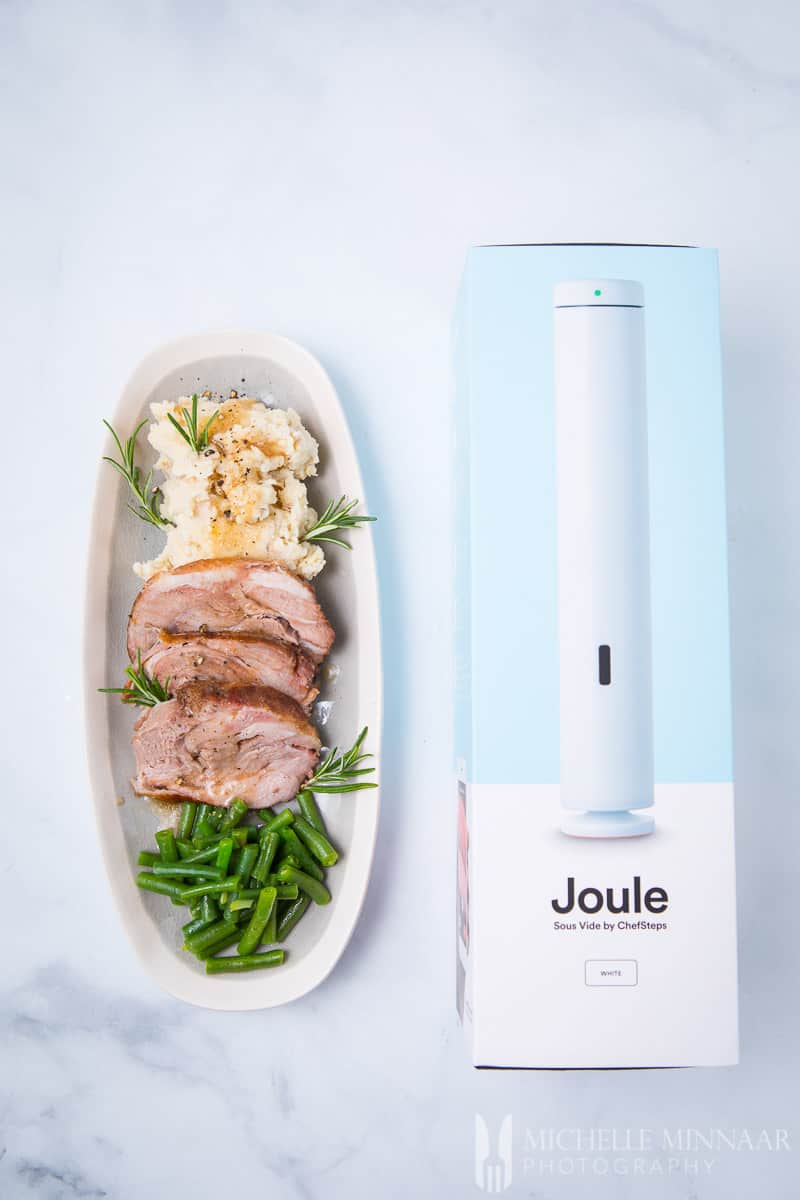 A plate of sous vide lamb shoulder with greens beans next to the Joule box