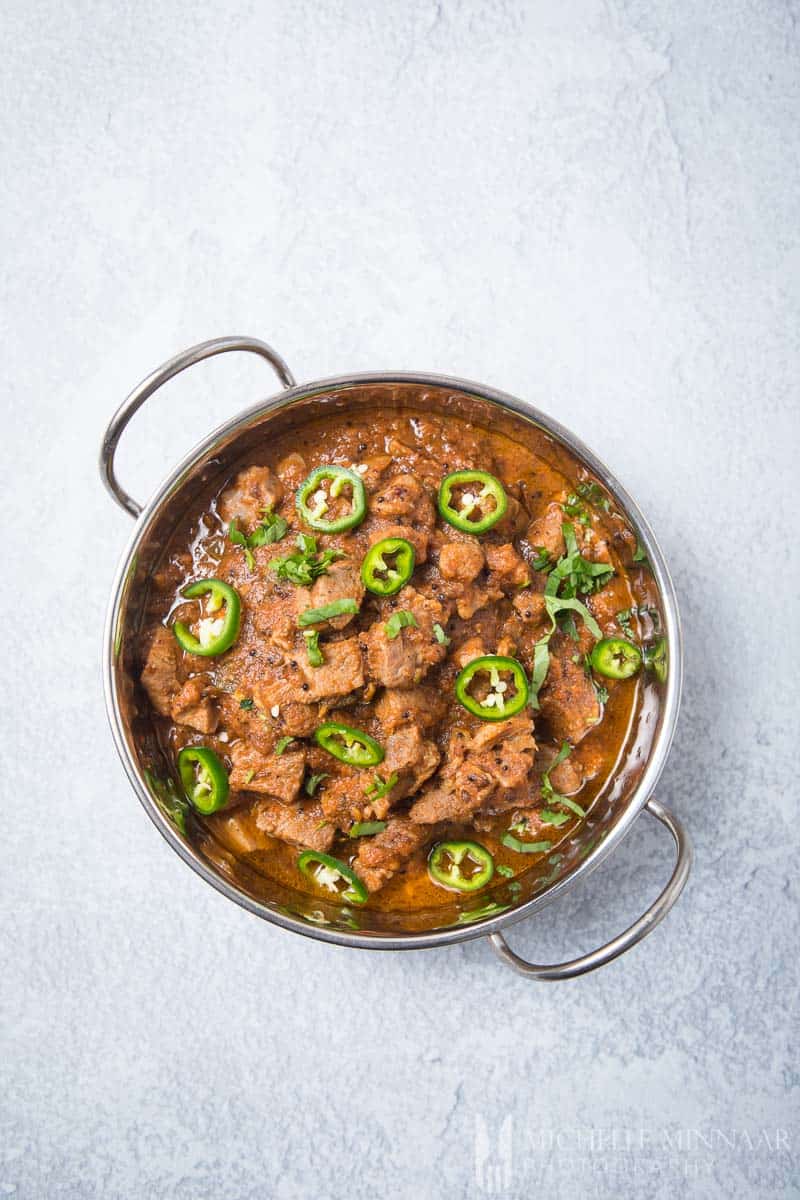 A bowl of browned lamb with jalepenos on top 