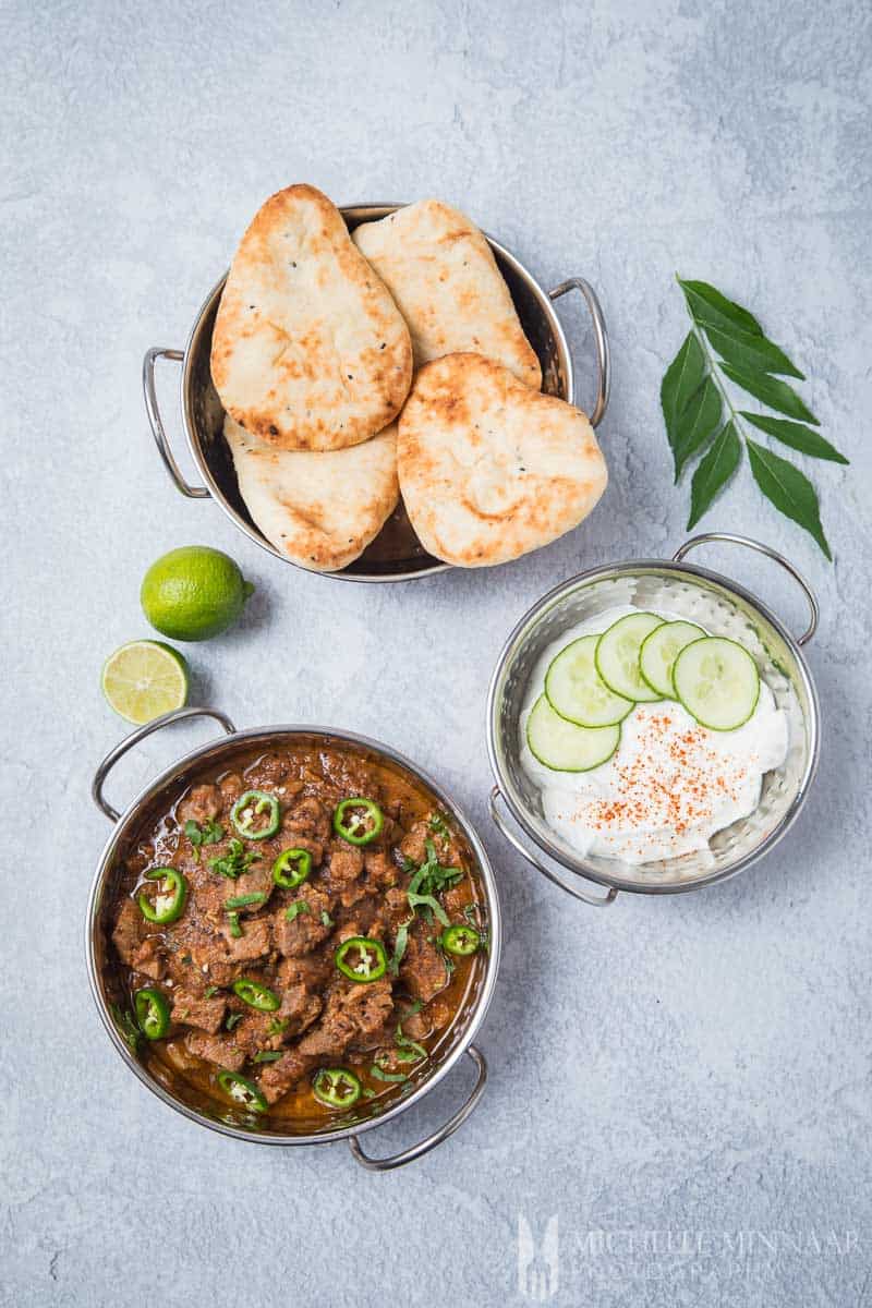 An indian meal, lamb bhuna, naan and raita