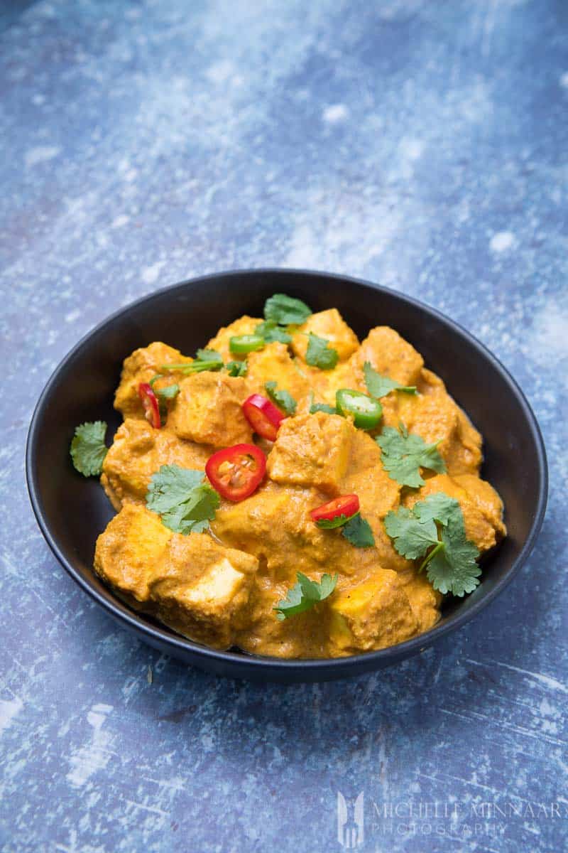 A bowl of paneer korma - Cubes of paneer in an orange sauce 