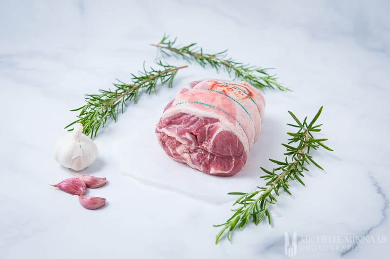 A raw rack of lamb and rosemary and garlic on a counter