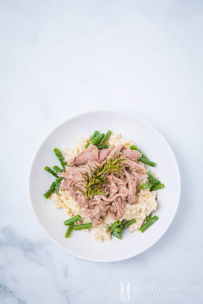 Sliced up lamb on top of mashed potatoes and greenbeans