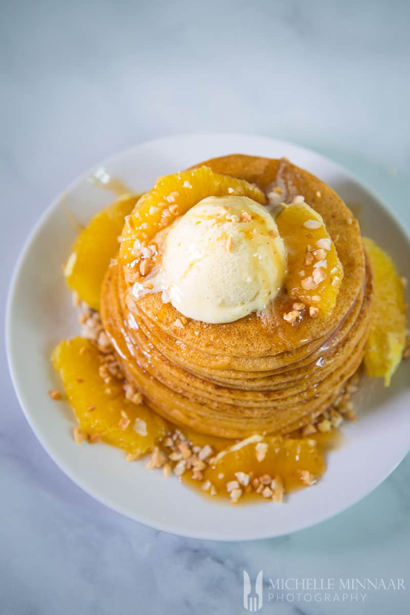 A high stack of vegan sweet potato pancakes with peaches and a scoop of ice cream in top 