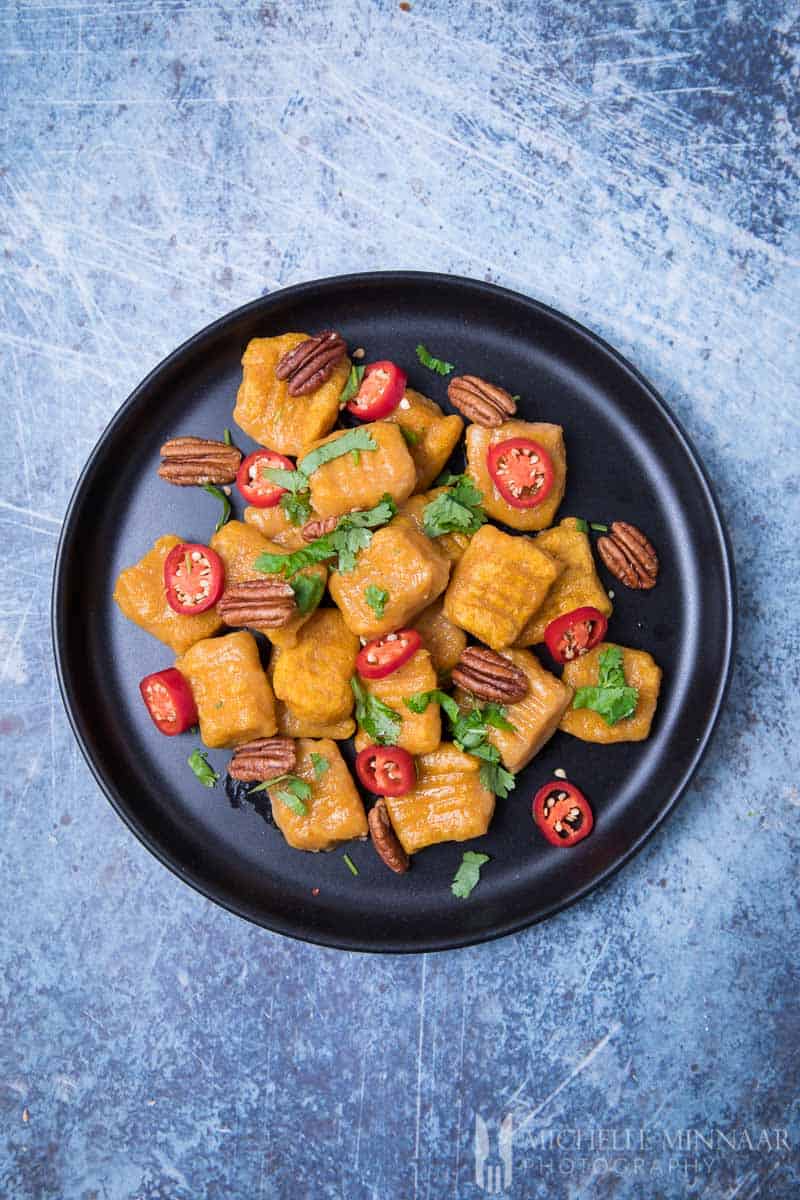 A bowl of vegan sweet potato gnocchi with tomatoes and nuts as garnish