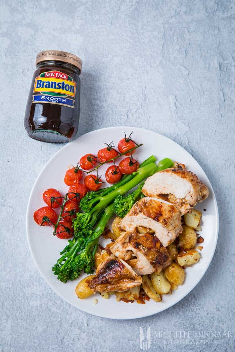 A plate of chicken ballotine with broccoli and tomatoes with a jar of Branston smooth next to it