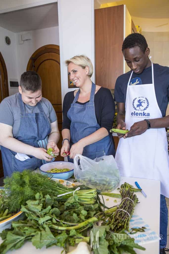 Three people in a kitchen peeling beans 