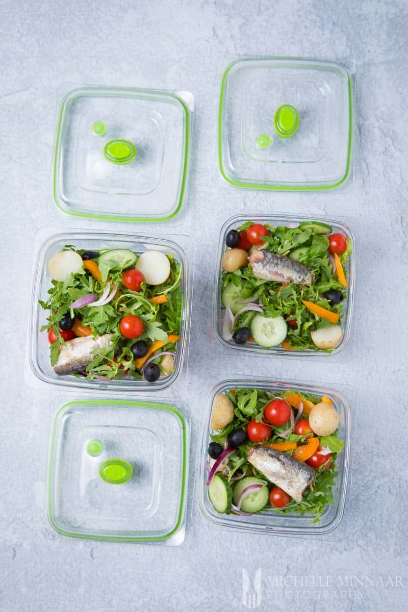 Three salad containers with sardines and salad in them