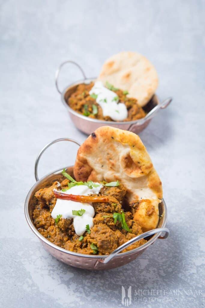 achar gosht in silver bowls with naan next to it 