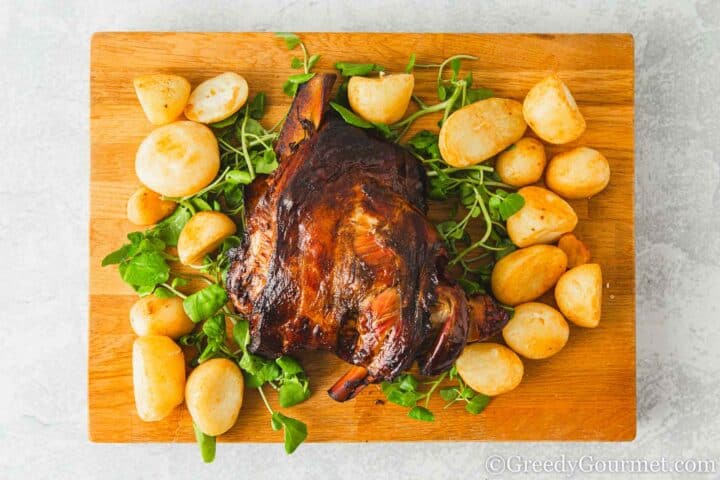 Slow roast lamb shoulder on a wooden board with potatoes.