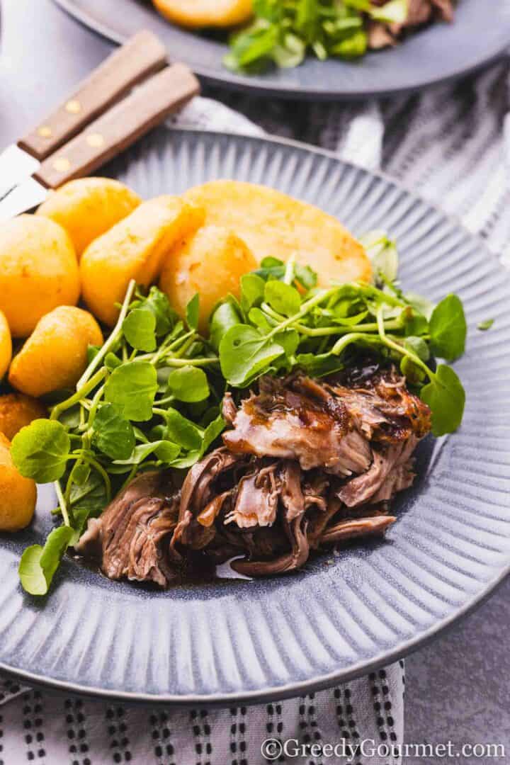 slow roast lamb shoulder served with potatoes and greens.