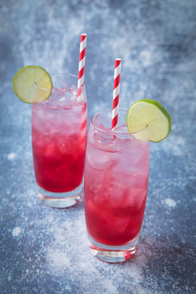 Two glasses of red and clear long beach iced tea with lime wheels as garnish and a red and white straw