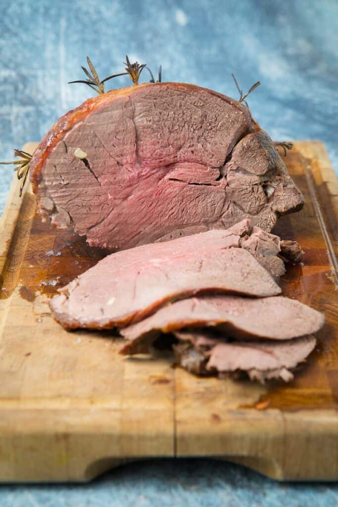 A large piece of roast venison on a cutting board cut in half 