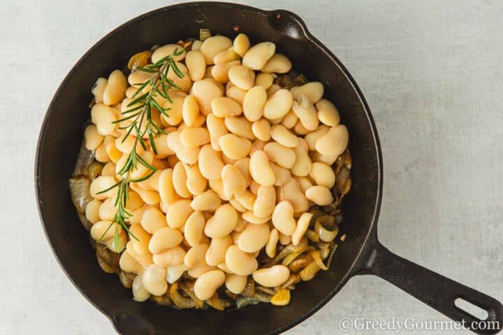 onion, butter beans and rosemary in a pan.
