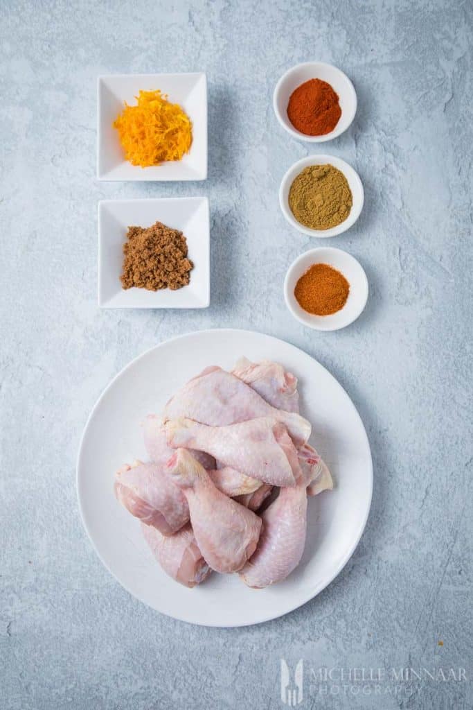 Raw chicken drumsticks and bowls of spices on a counter