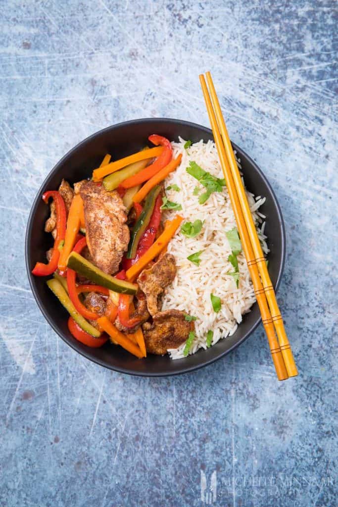  A bowl of sweet chili chicken stir fry and rice with chopsticks