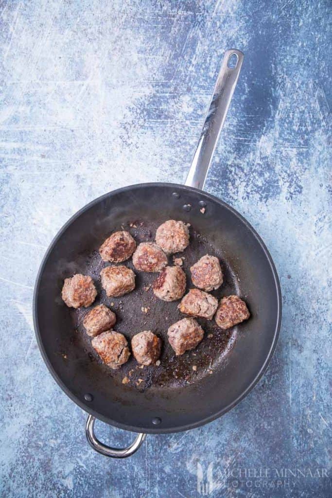 Meatballs being fried in a saute pan
