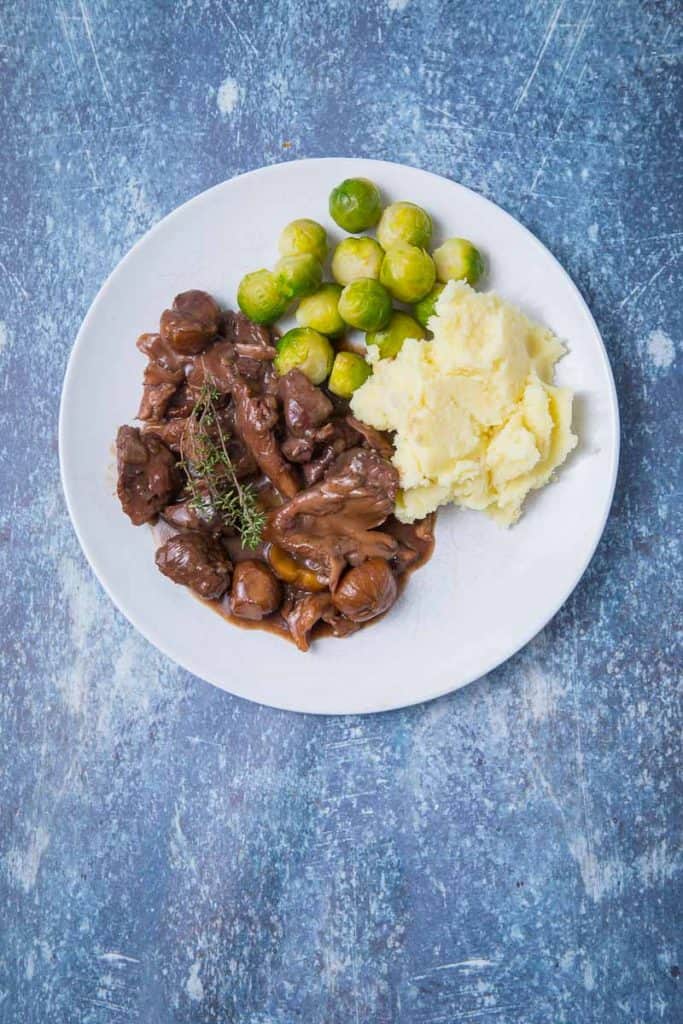 A plate of game casserole, mashed potatoes and brussel sprouts