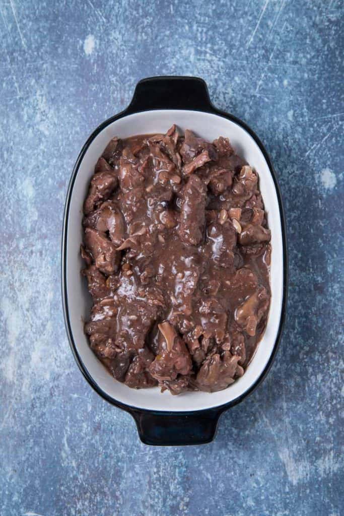 A pile of game meat covered in a brown sauce in a pan