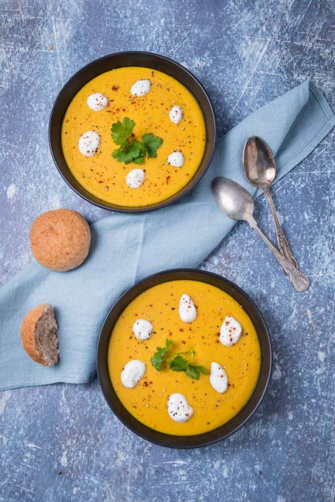 Two bowls of yellow Lebanese Lentil Soup with two spoons and bread