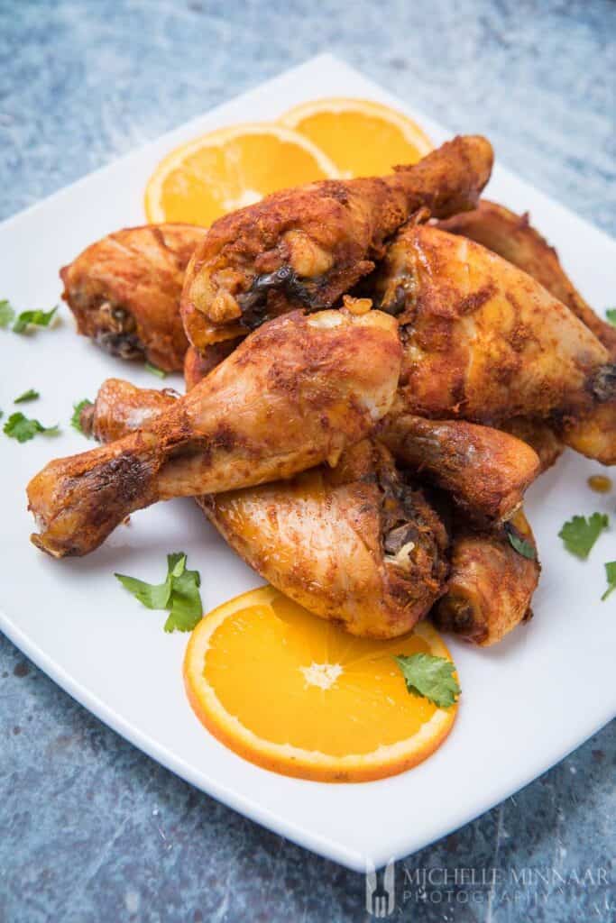 A pile of browned Marinated Chicken Drumsticks with lemons on a plate