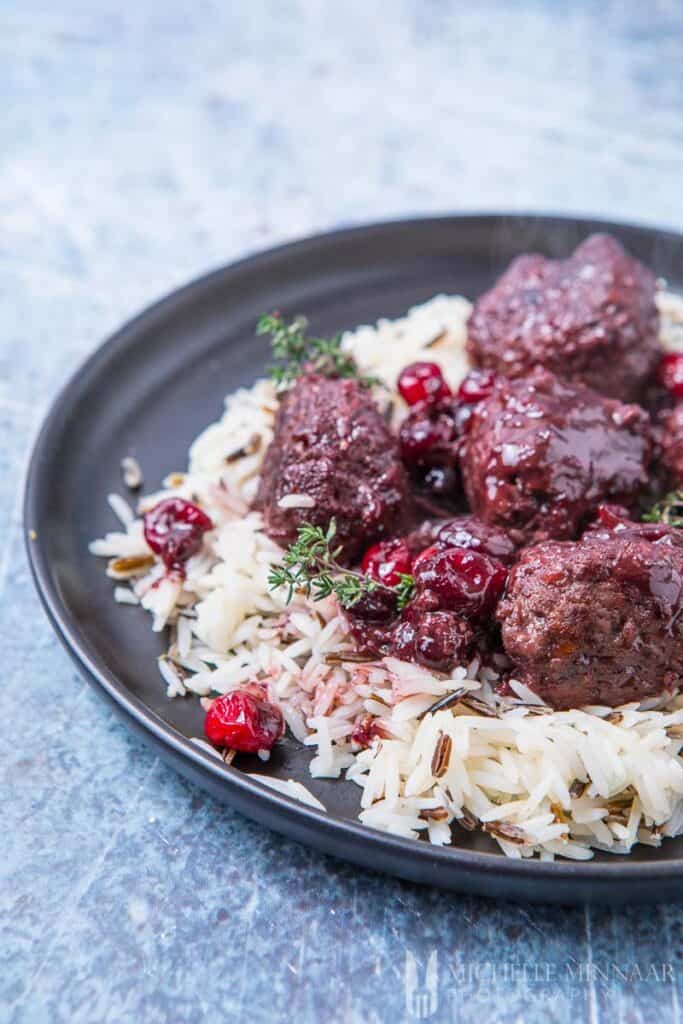 A finished plate of venison meatballs covered in a cranberry sauce over rice