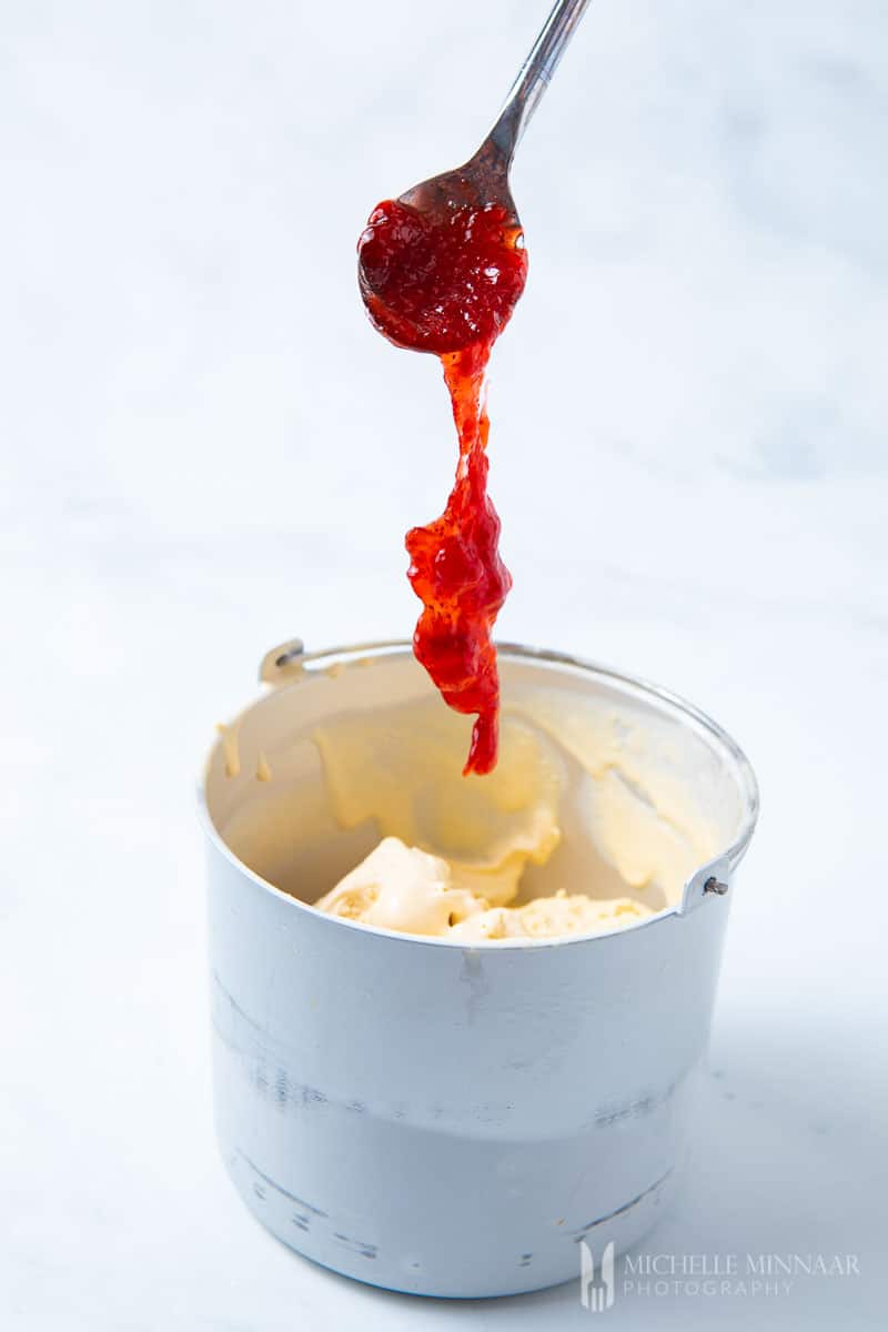 A spoon of jelly being dropped into the ice cream 