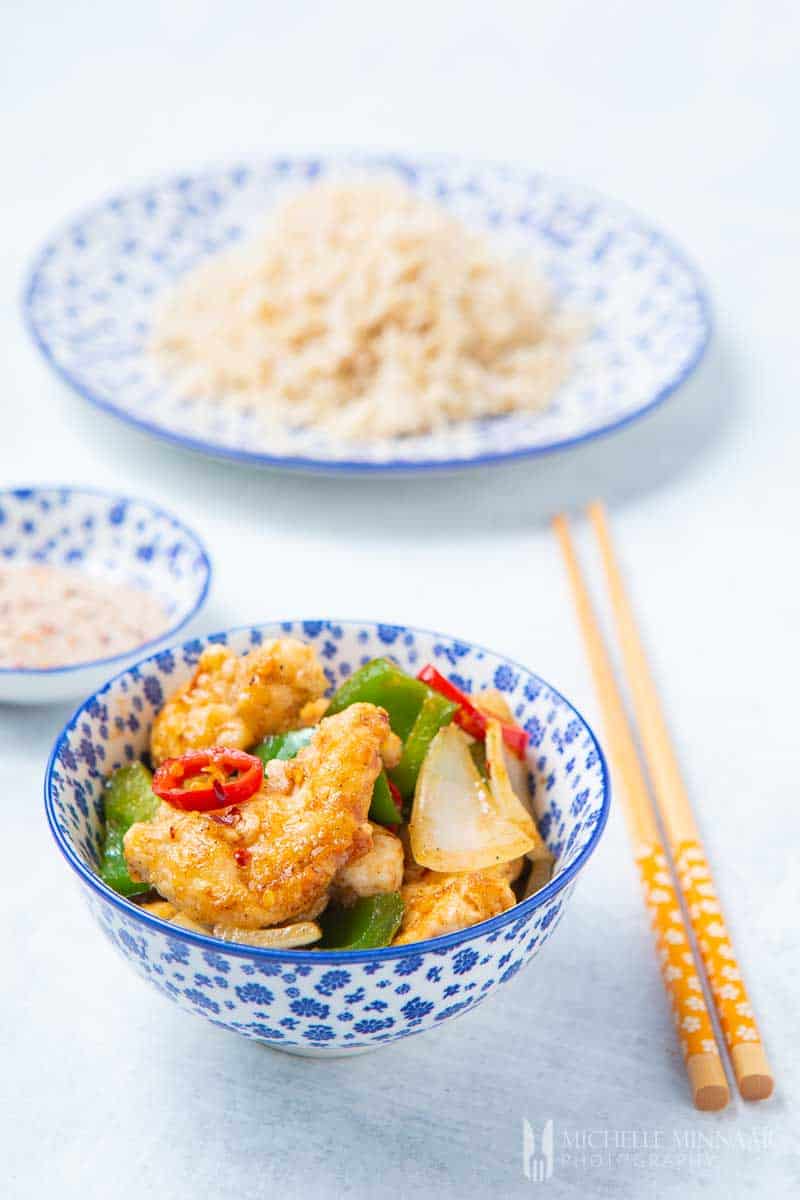 A bowl of salt and chili chicken with chopsticks and a plate of rice