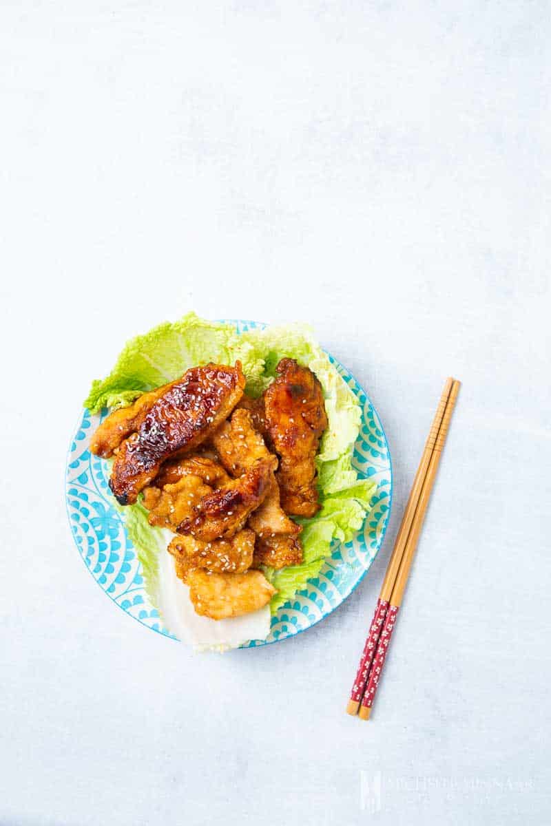 A plate of marmite chicken with a brown sauce on a bed of lettuce, 