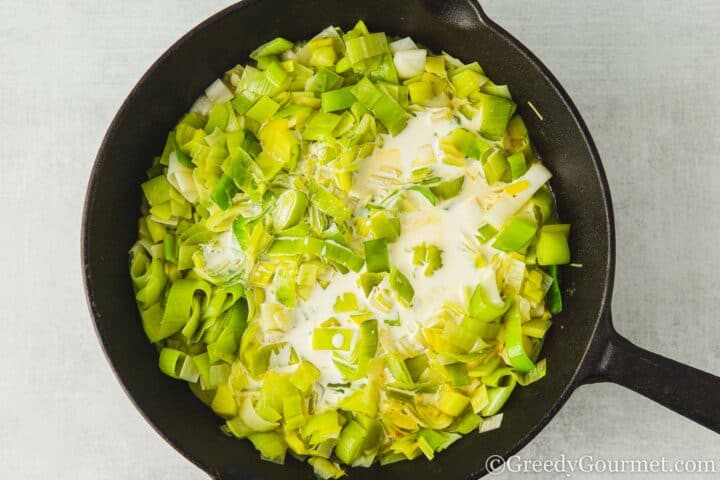 Adding cream to leeks in a pan.