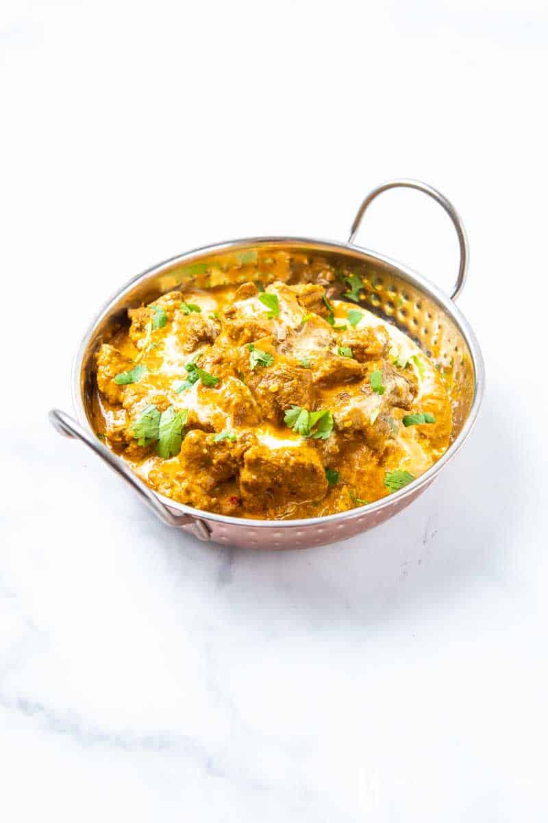 A bowl of beef korma, beef and brown curry sauce in a silver bowl