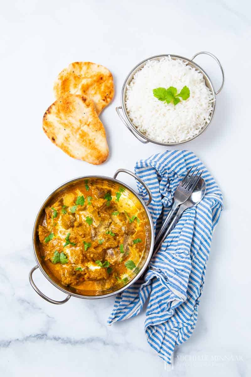 A bowl of beef korma, naan bread and white rice 