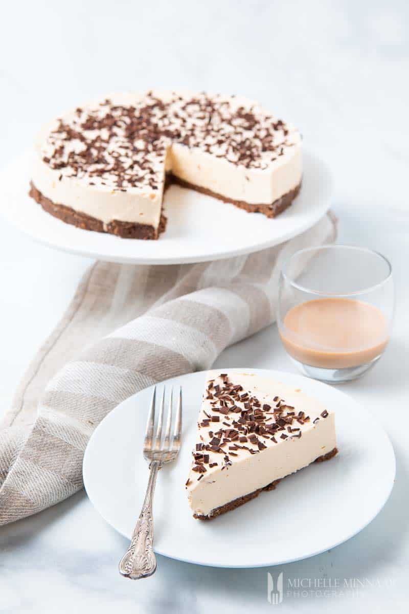 An amarula cheesecake with a slice removed and a glass of cream liquor