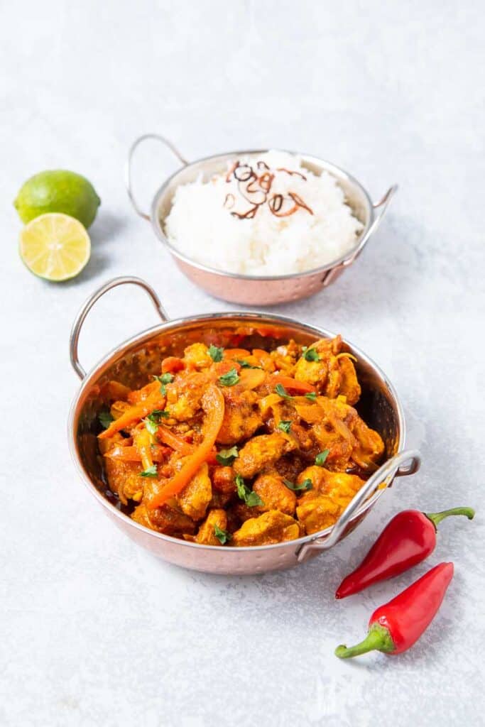 Bowl of Chicken Jalfrezi, white rice, whole lime and whole red peppers 